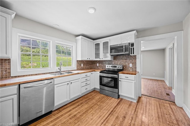 kitchen with stainless steel appliances, a sink, light wood-style floors, white cabinets, and glass insert cabinets