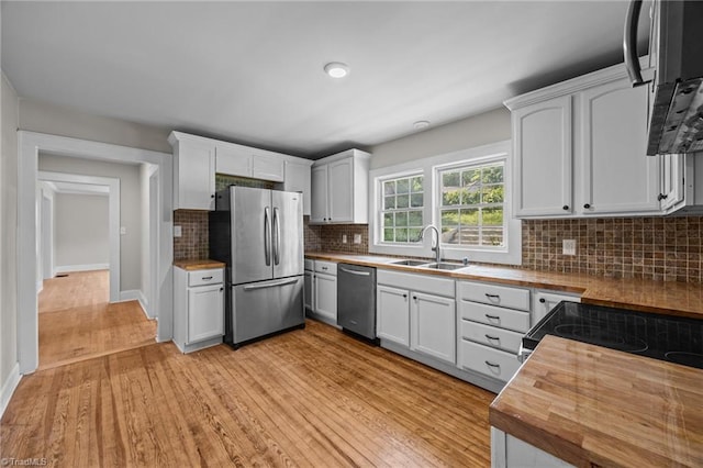 kitchen with appliances with stainless steel finishes, wood counters, a sink, light wood finished floors, and tasteful backsplash