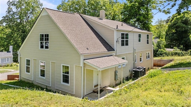 rear view of house with a shingled roof, a chimney, and central AC unit