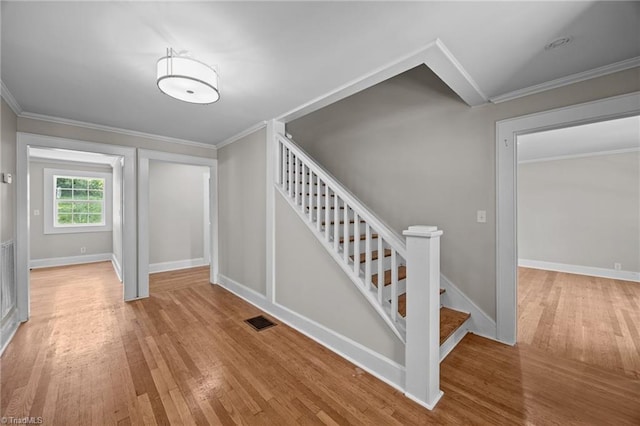 stairway with wood finished floors, baseboards, and ornamental molding