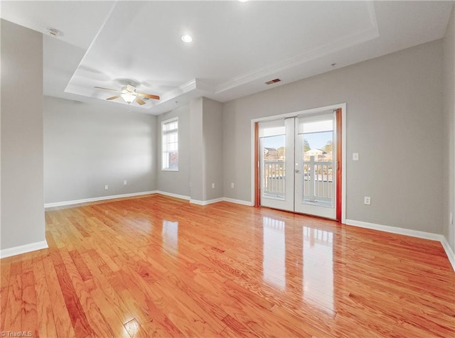 empty room featuring a tray ceiling, ceiling fan, light hardwood / wood-style flooring, and french doors