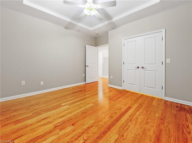 unfurnished bedroom with ceiling fan, a closet, light hardwood / wood-style flooring, and a tray ceiling