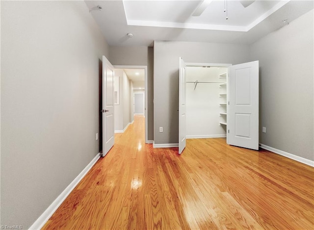 unfurnished bedroom with ceiling fan, a raised ceiling, light wood-type flooring, and a closet