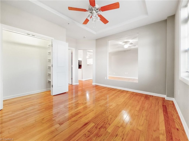 unfurnished bedroom featuring a raised ceiling, a closet, light hardwood / wood-style flooring, and ceiling fan