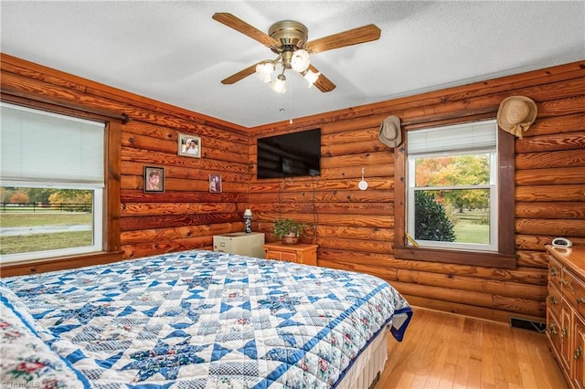 bedroom featuring light wood-type flooring, ceiling fan, and log walls