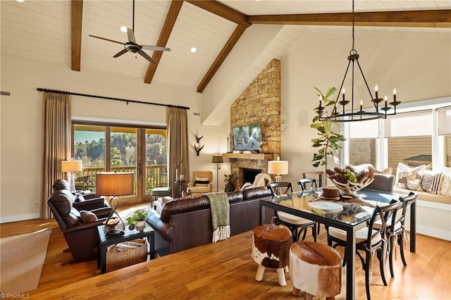 dining area featuring ceiling fan with notable chandelier, high vaulted ceiling, beamed ceiling, hardwood / wood-style floors, and a stone fireplace