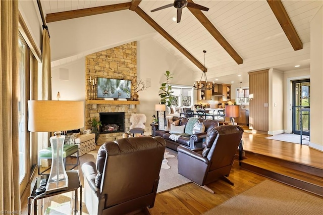 living room with a stone fireplace, light hardwood / wood-style flooring, high vaulted ceiling, beamed ceiling, and ceiling fan with notable chandelier