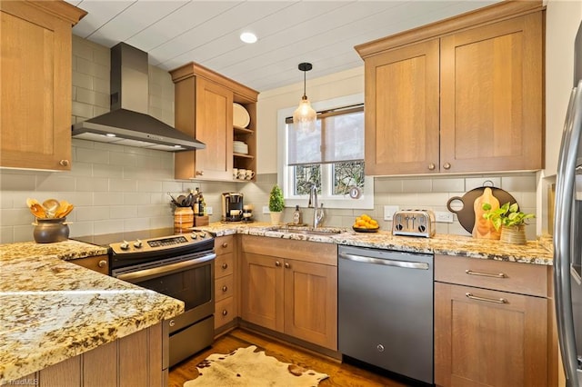 kitchen featuring light stone counters, sink, wall chimney range hood, and appliances with stainless steel finishes