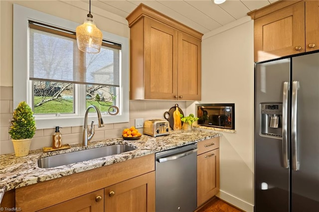 kitchen with pendant lighting, backsplash, sink, light stone countertops, and stainless steel appliances