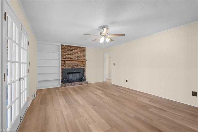 unfurnished living room featuring built in shelves, a textured ceiling, light hardwood / wood-style flooring, ceiling fan, and a fireplace