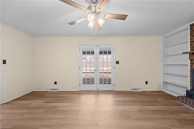 empty room with french doors, built in features, light hardwood / wood-style floors, and a brick fireplace