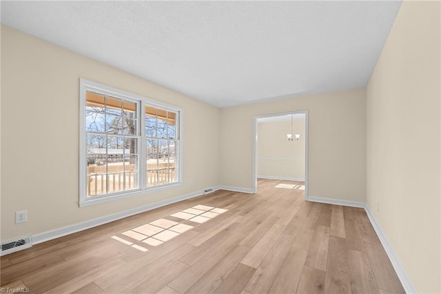 empty room featuring an inviting chandelier and light hardwood / wood-style flooring