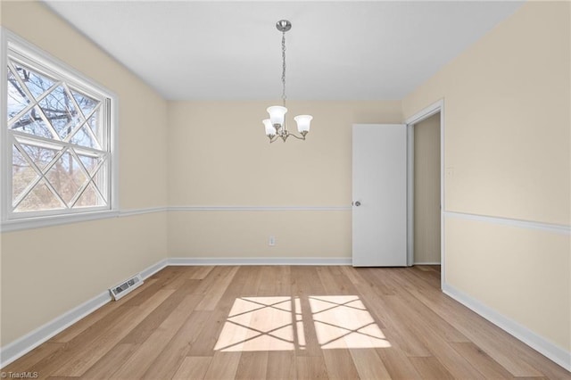 spare room featuring a chandelier and light wood-type flooring