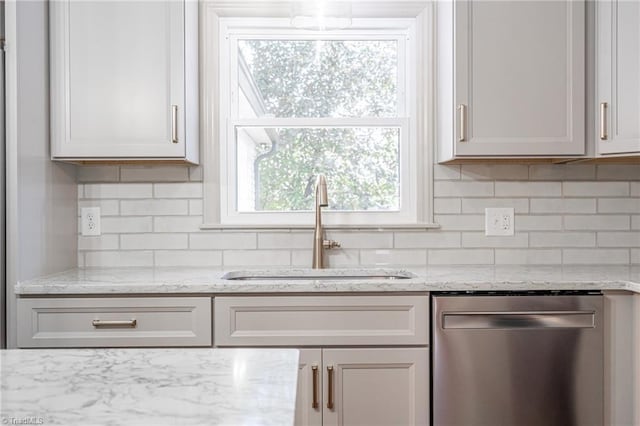 kitchen featuring tasteful backsplash, light stone countertops, white cabinets, stainless steel dishwasher, and sink