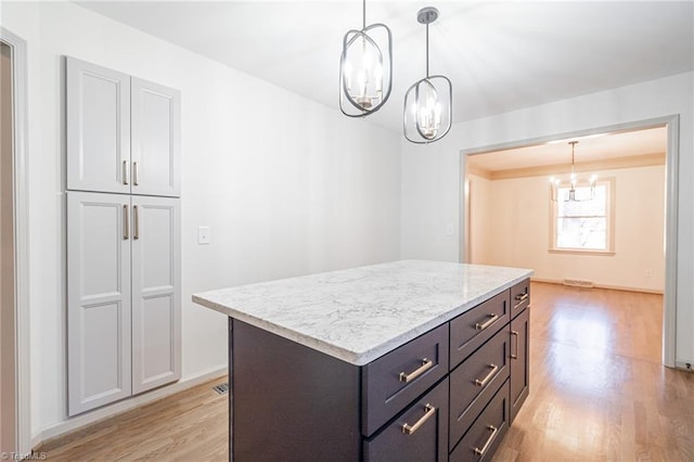 kitchen with light stone countertops, decorative light fixtures, light hardwood / wood-style floors, a chandelier, and a kitchen island