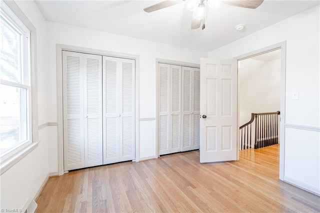 unfurnished bedroom with multiple windows, two closets, ceiling fan, and light hardwood / wood-style flooring