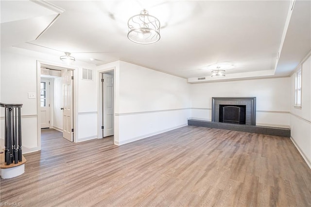 unfurnished living room featuring a brick fireplace, light hardwood / wood-style floors, and a raised ceiling