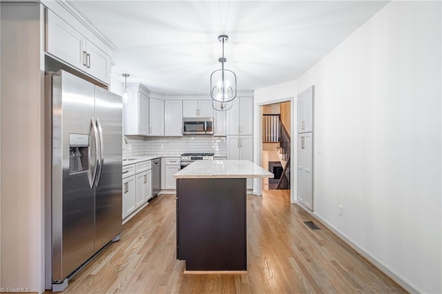 kitchen with decorative light fixtures, a kitchen island, backsplash, appliances with stainless steel finishes, and white cabinets