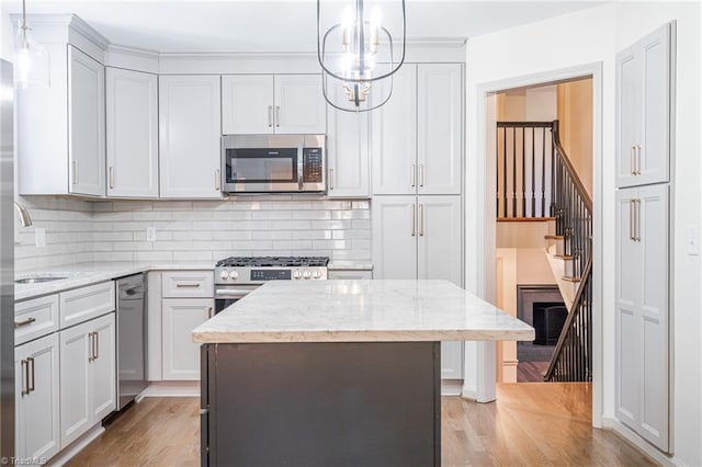 kitchen with light hardwood / wood-style flooring, stainless steel appliances, light stone counters, decorative light fixtures, and a center island