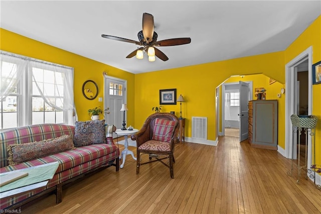 living area with light wood-type flooring, visible vents, arched walkways, and baseboards