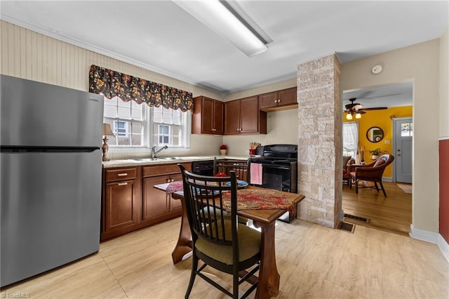 kitchen with ceiling fan, a sink, light countertops, black appliances, and decorative columns