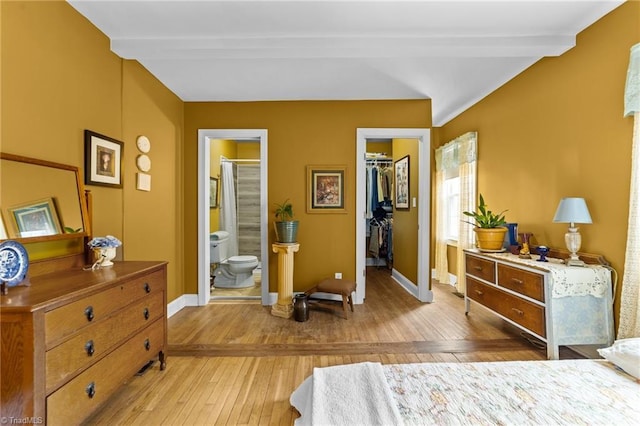 bedroom with baseboards, beam ceiling, a walk in closet, light wood-type flooring, and a closet