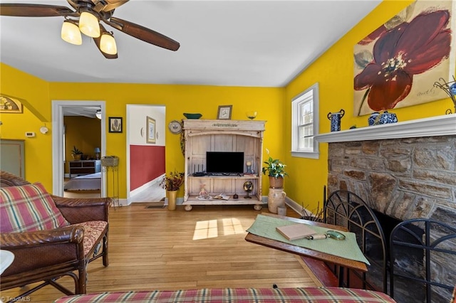 living area with a stone fireplace, wood finished floors, and baseboards