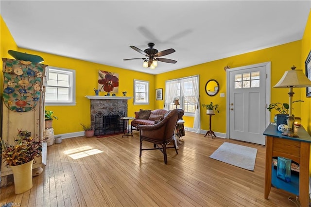 living room featuring a wealth of natural light, wood-type flooring, a stone fireplace, and baseboards