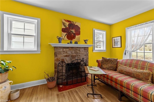 living area featuring baseboards, a stone fireplace, hardwood / wood-style flooring, and a healthy amount of sunlight