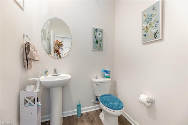 half bathroom with a sink, toilet, baseboards, and wood finished floors