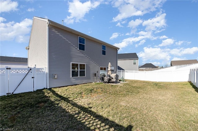 rear view of property featuring a lawn, a fenced backyard, and a gate