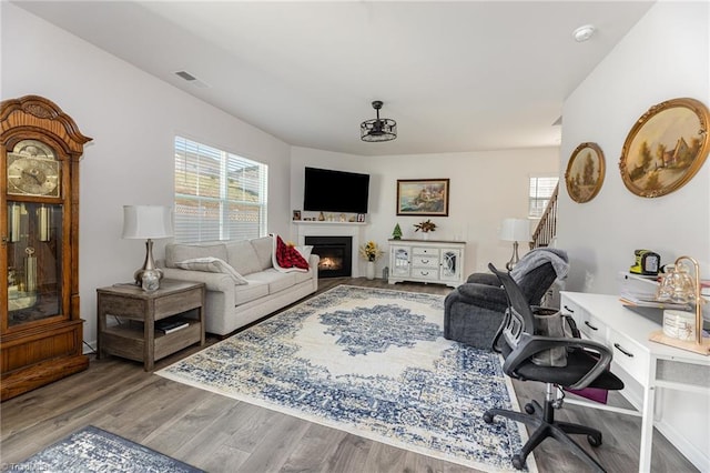 living area featuring visible vents, a lit fireplace, and wood finished floors