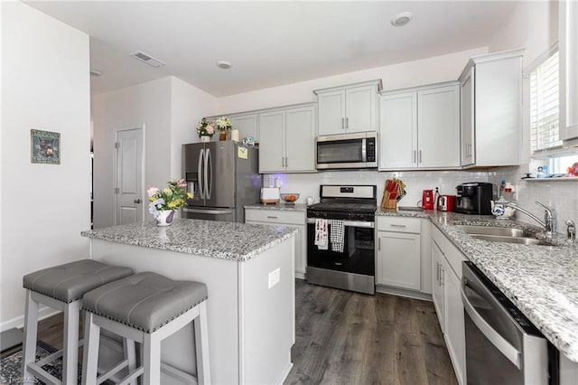 kitchen with visible vents, a breakfast bar area, decorative backsplash, stainless steel appliances, and a sink