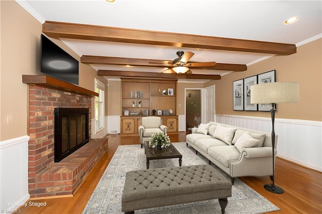 living room with crown molding, a brick fireplace, hardwood / wood-style flooring, beamed ceiling, and ceiling fan