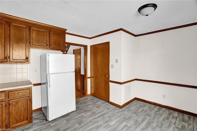 kitchen with white refrigerator, crown molding, tasteful backsplash, and light hardwood / wood-style flooring