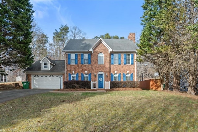 colonial house with driveway, a front yard, an attached garage, brick siding, and a chimney