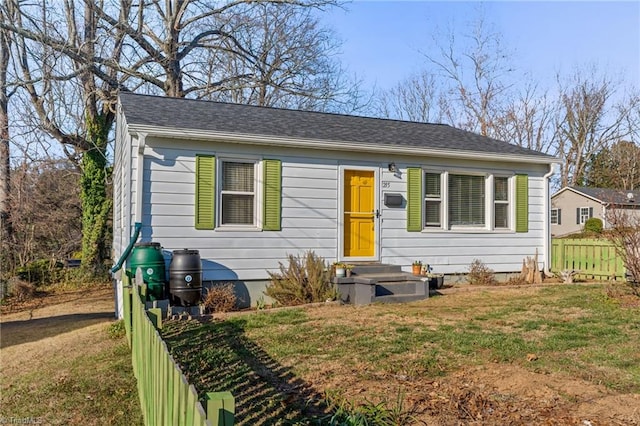 bungalow-style house with roof with shingles, fence, and a front lawn