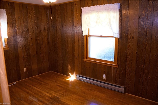 empty room featuring hardwood / wood-style floors, baseboard heating, wooden walls, and ceiling fan