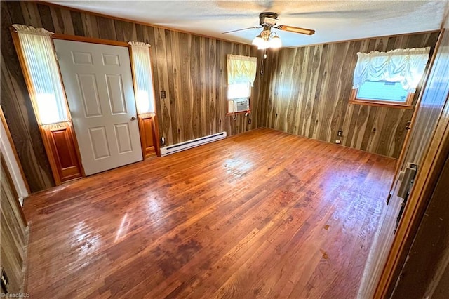 unfurnished bedroom featuring wooden walls, hardwood / wood-style flooring, baseboard heating, and ceiling fan