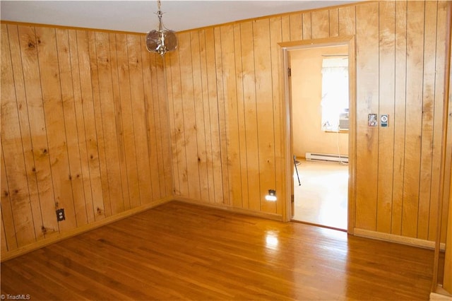 unfurnished room with wooden walls, a baseboard heating unit, and hardwood / wood-style flooring