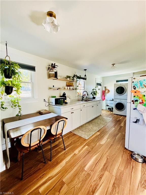 kitchen featuring white appliances, sink, light hardwood / wood-style flooring, white cabinets, and stacked washer and dryer