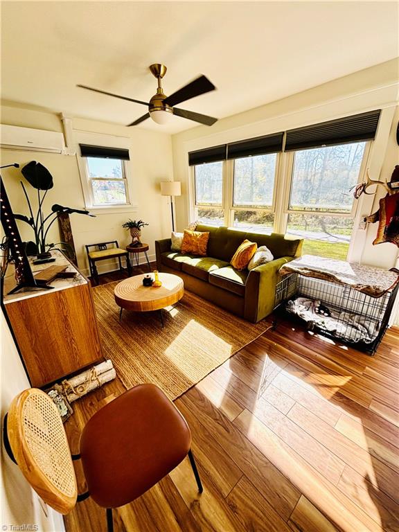 living room with a wall mounted air conditioner, hardwood / wood-style floors, a wealth of natural light, and ceiling fan