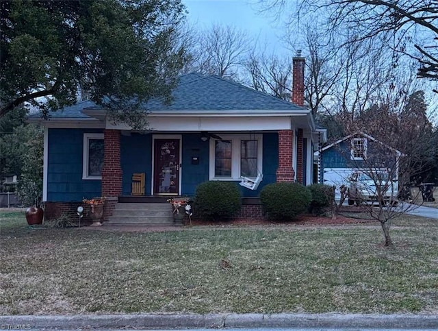 bungalow-style home featuring roof with shingles, a porch, a front lawn, and a chimney