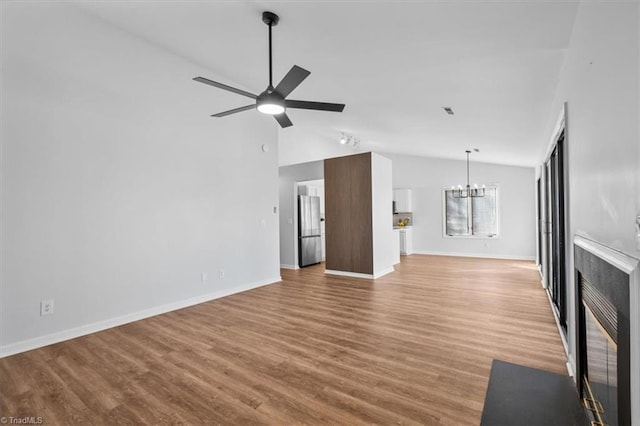 unfurnished living room with a fireplace with flush hearth, vaulted ceiling, wood finished floors, baseboards, and ceiling fan with notable chandelier