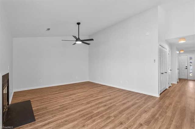 unfurnished living room featuring light wood-type flooring, a glass covered fireplace, visible vents, and vaulted ceiling