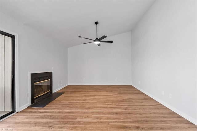 unfurnished living room featuring baseboards, lofted ceiling, a fireplace with flush hearth, ceiling fan, and light wood-type flooring