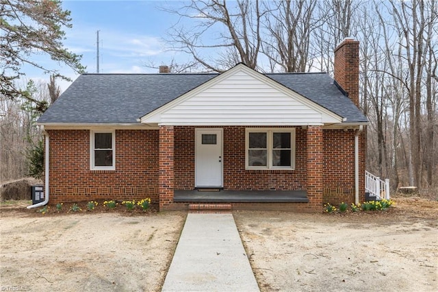 bungalow-style home featuring brick siding, covered porch, a chimney, and roof with shingles