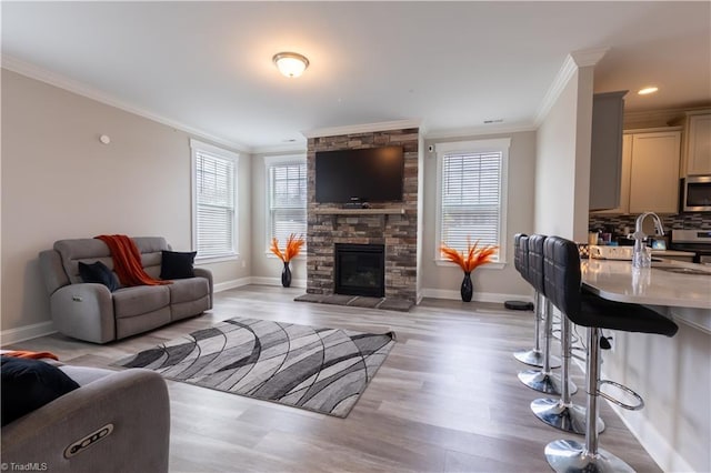 living area with baseboards, a stone fireplace, light wood finished floors, and crown molding