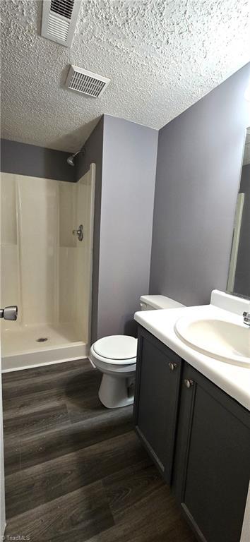 bathroom featuring walk in shower, a textured ceiling, vanity, hardwood / wood-style flooring, and toilet