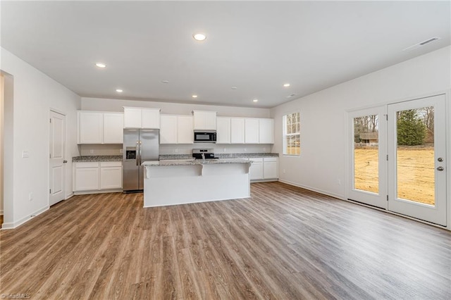 kitchen with white cabinetry, stainless steel appliances, light stone countertops, light hardwood / wood-style floors, and a center island with sink